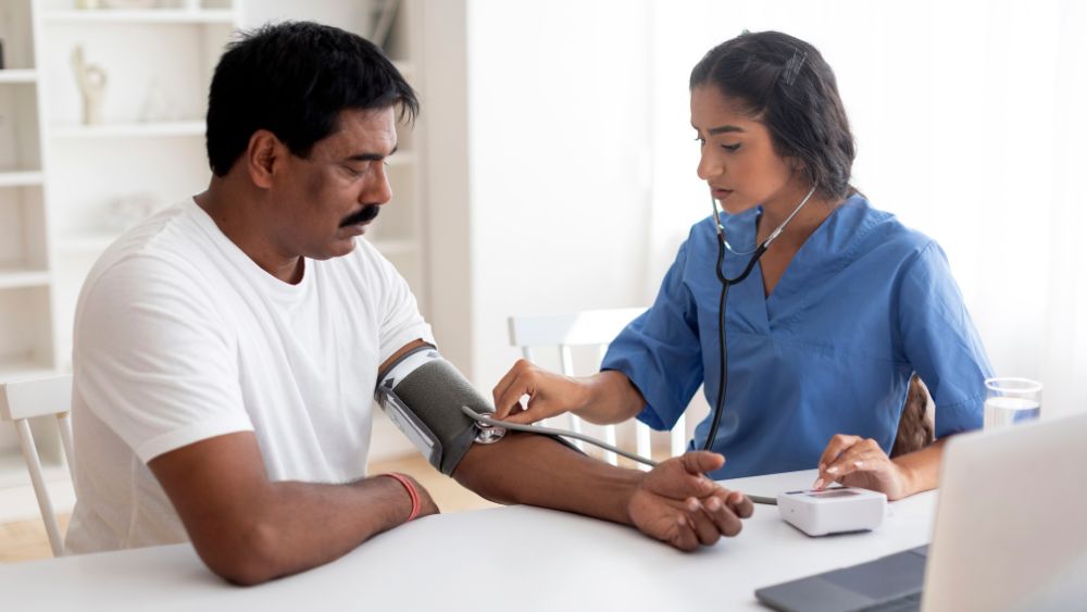 Nurse checking blood pressure at home for patient during home blood testing and healthcare service.